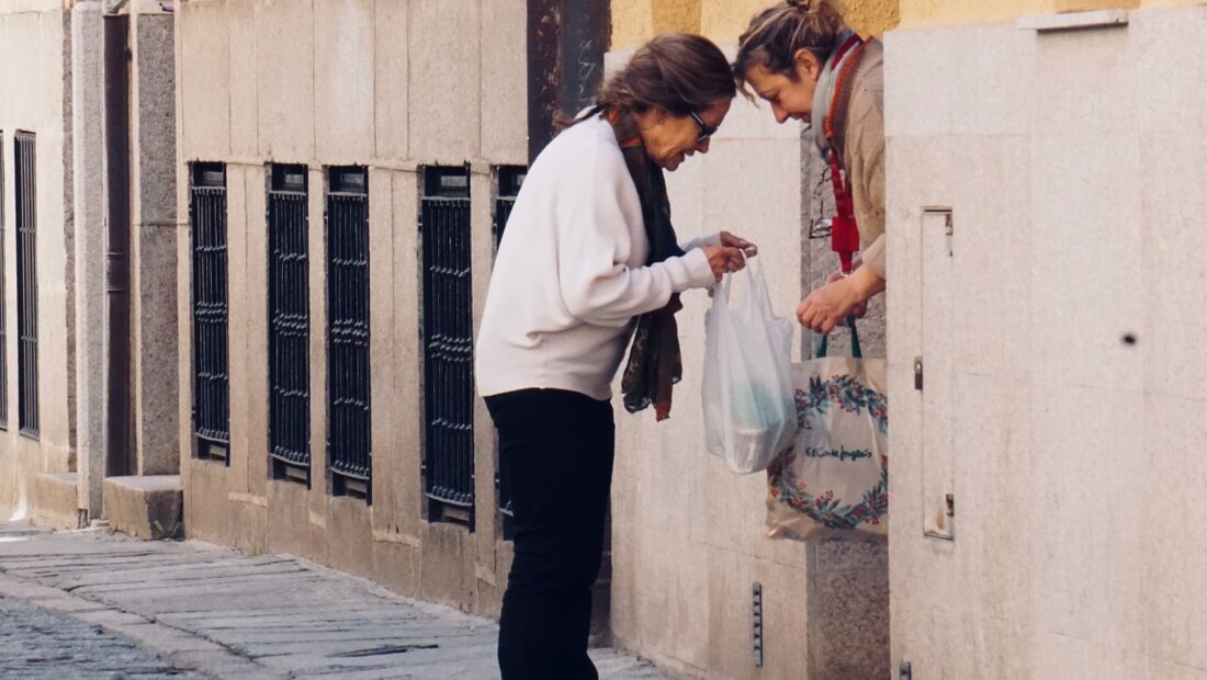 A neighbour hands over a bag of groceries at the front door