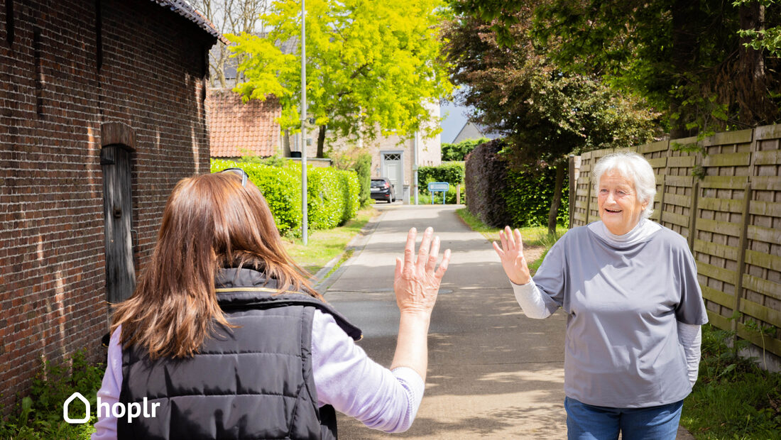 Two neighbours wave to each other in their street